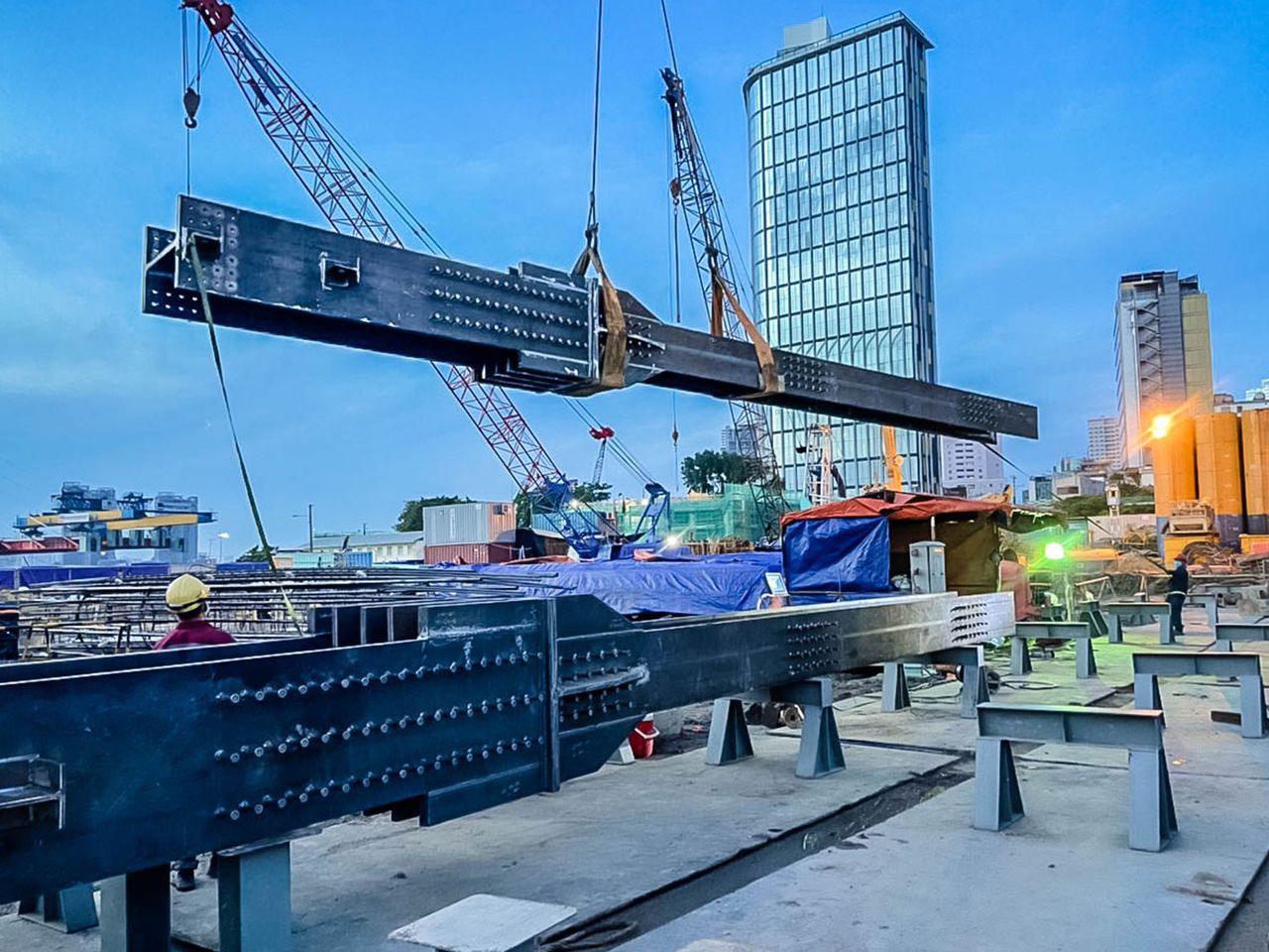 Built-up steel kingpost being lifted on a high-rise basement site in Ho Chi Minh City, with towers in the background